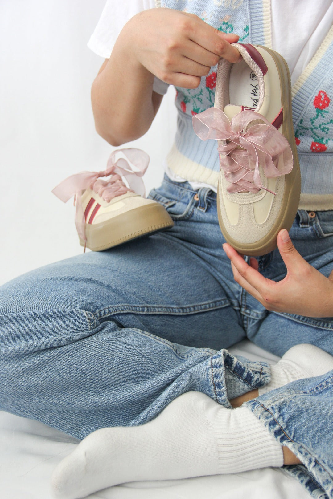 Model holding Tippies beige casual sneakers with burgundy stripes