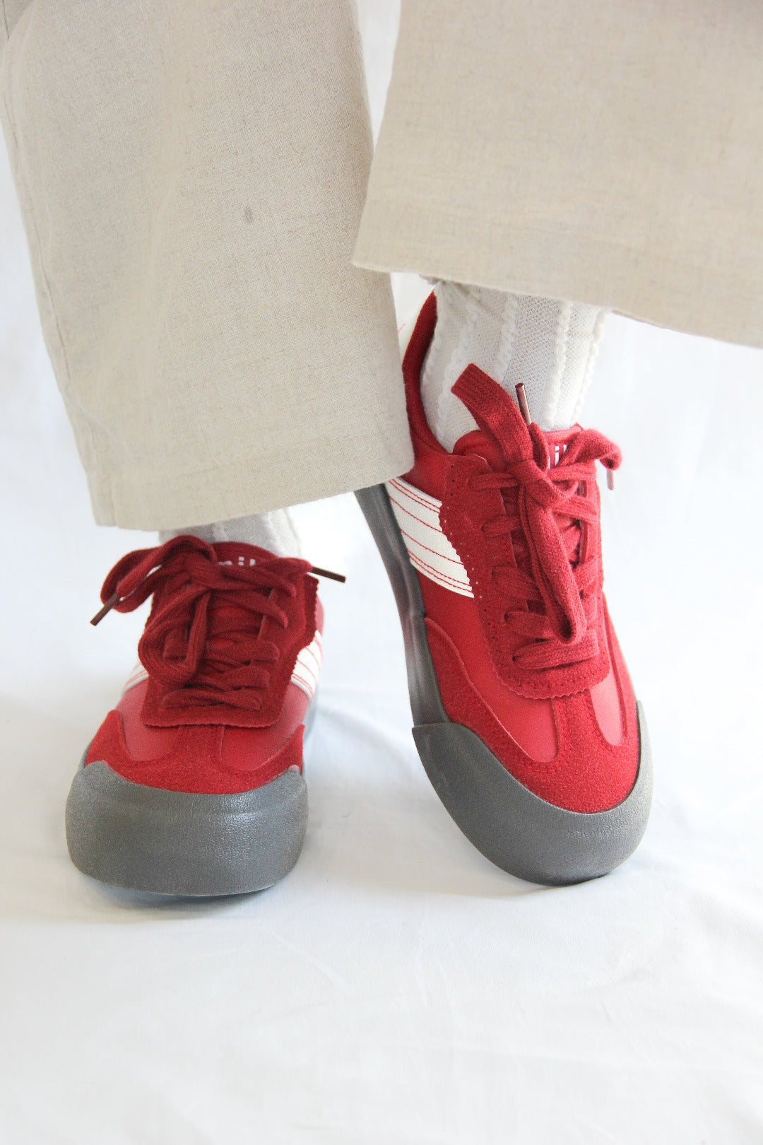 Side view of model wearing a pair of Jena Red Sneakers, standing.