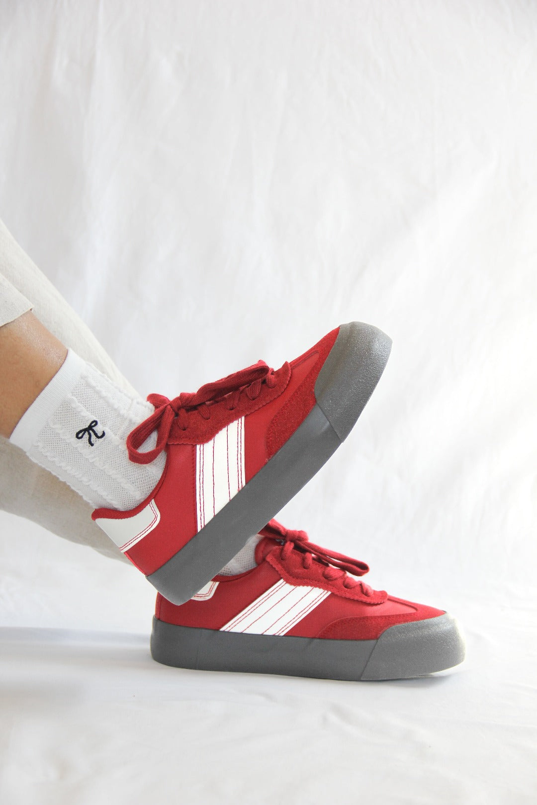 Side view of model wearing a pair of Jena Red Sneakers.