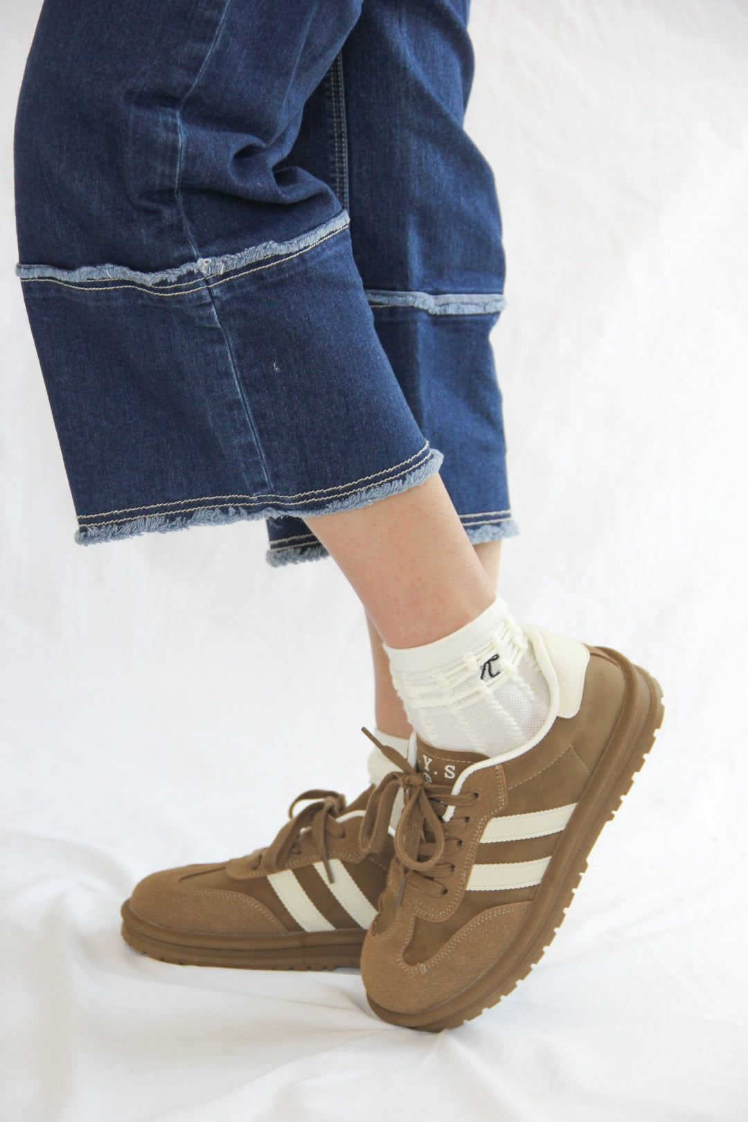 Side view of model wearing Essen Mocha Sneakers, with a rich mocha brown suede and mesh upper, white stripes, and a comfortable platform sole.